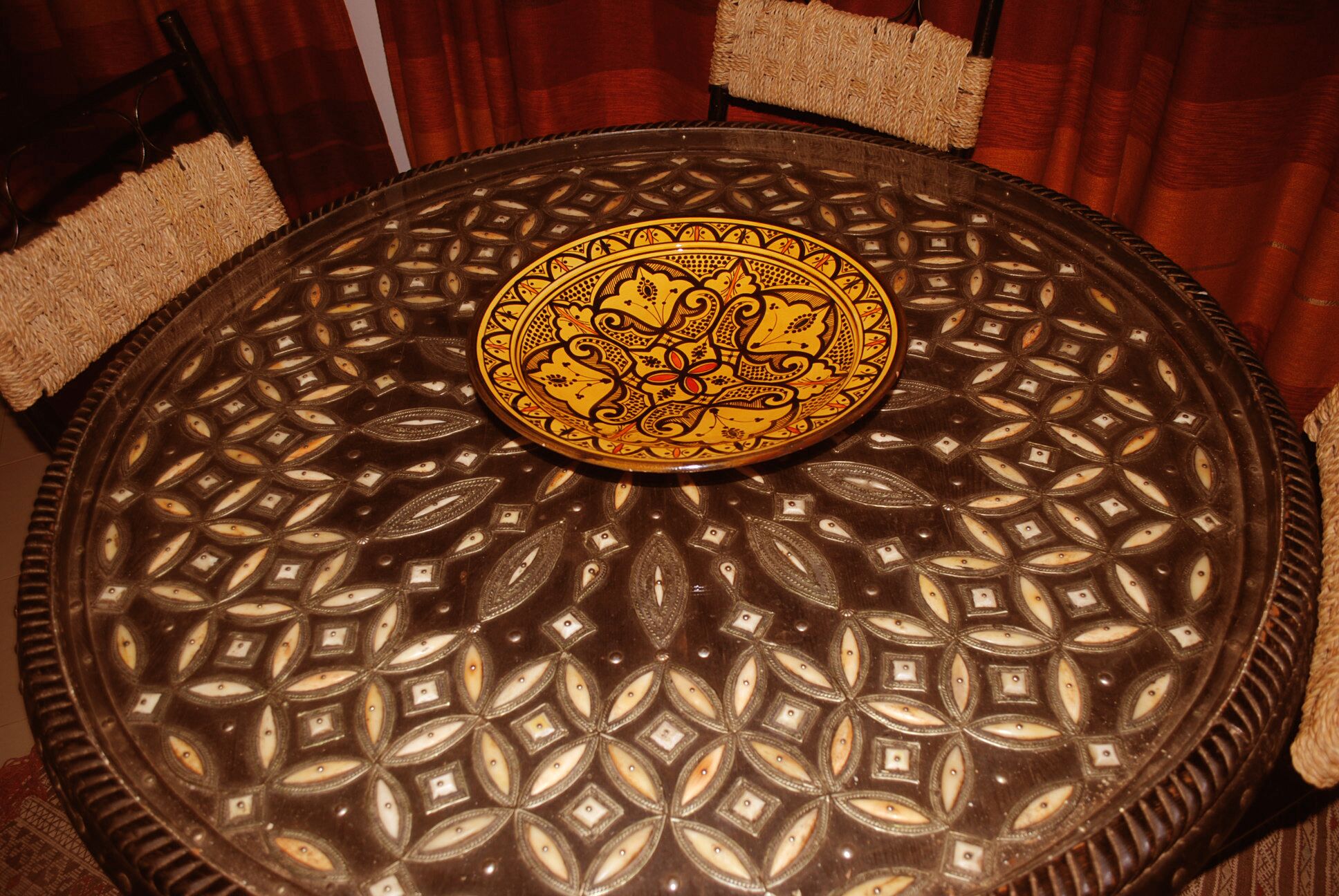 Una mesa redonda con cubierta de vidrio decorativa que presenta un patrón geométrico y una medalla central con diseños intrincados.