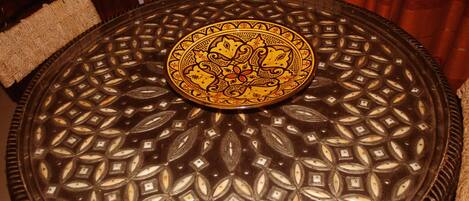 Una mesa redonda con cubierta de vidrio decorativa que presenta un patrón geométrico y una medalla central con diseños intrincados.