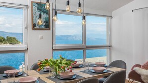 Een eethoek met uitzicht op de zee, een tafel gedekt met roze kommen en glazen, en een vaas met bloemen.