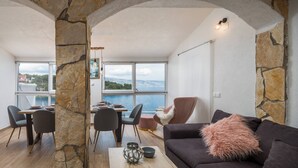 Een moderne woonkamer met stenen muren, een donkere bank, een houten salontafel en uitzicht op zee.