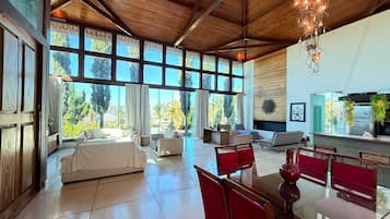 Amplia sala de estar con techo alto, ventanas grandes y comedor con sillas rojas.