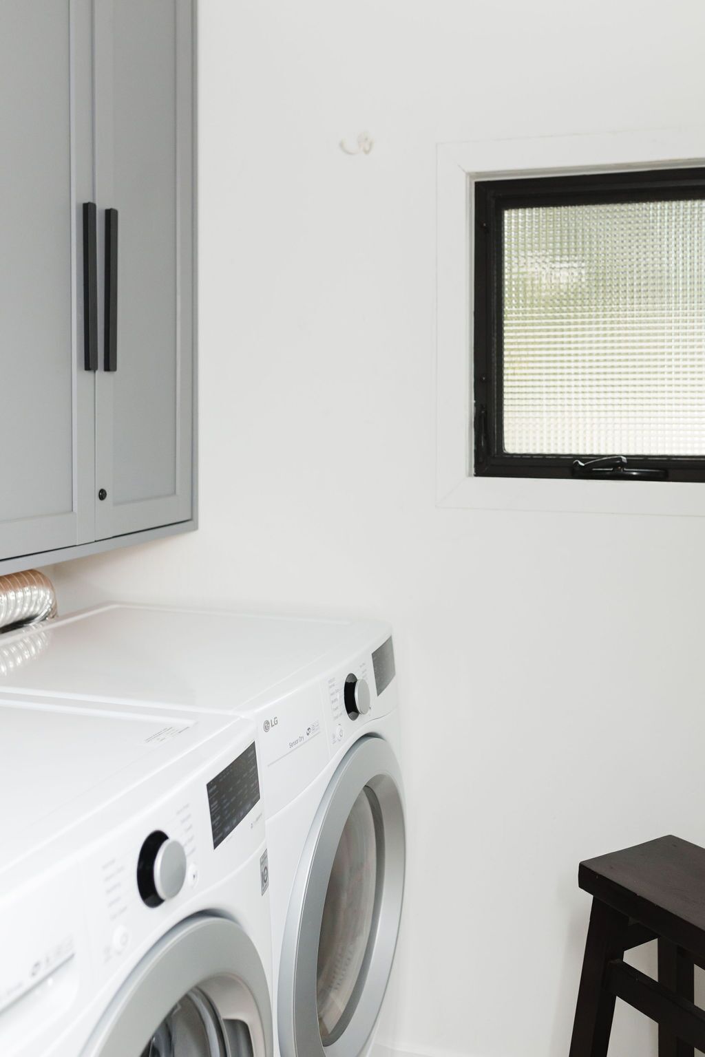 Une buanderie équipée d’un lave-linge à chargement frontal, d’un meuble et d’une fenêtre.