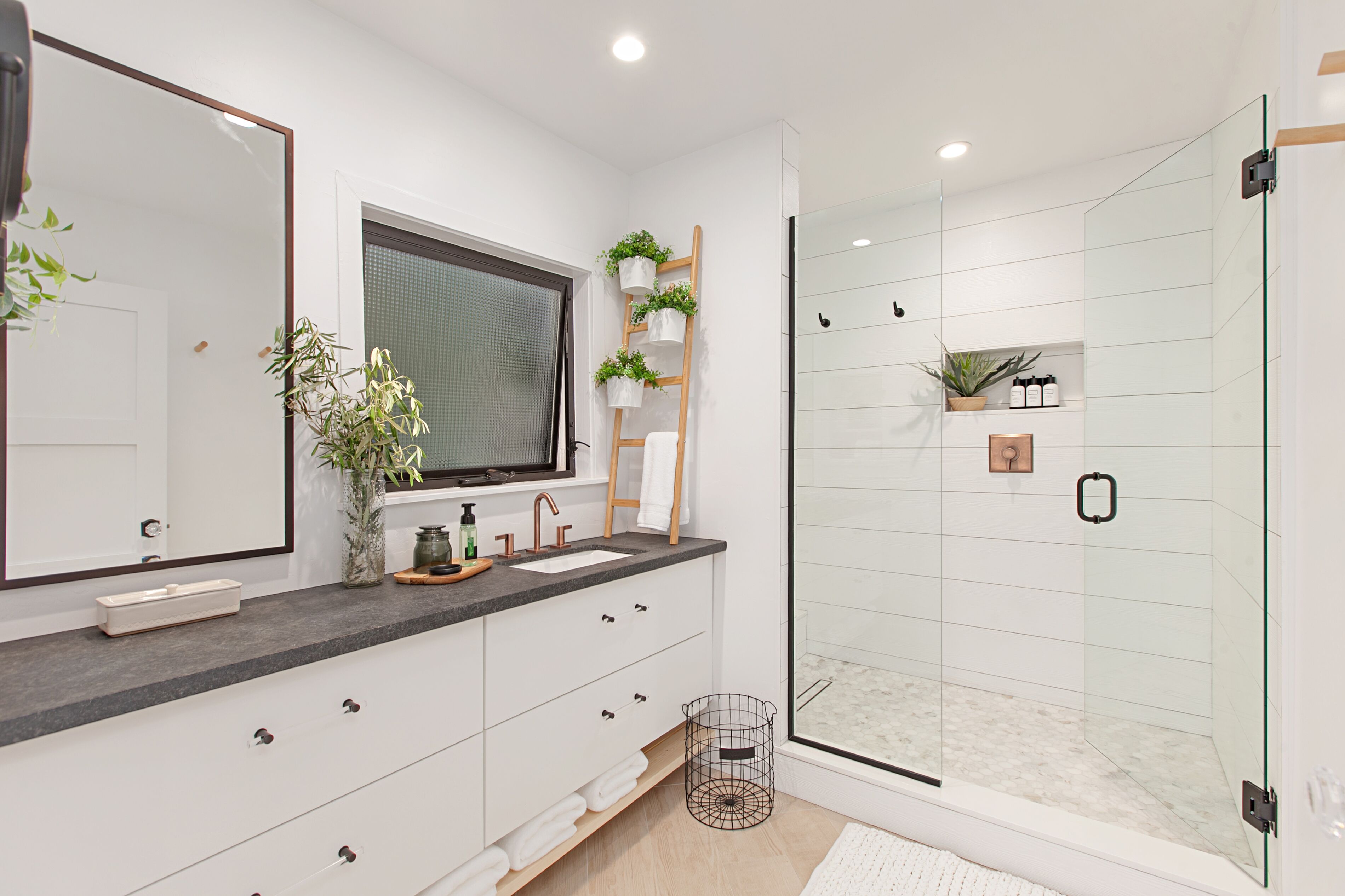 A modern bathroom with a glass shower enclosure, white cabinetry, and a large mirror.