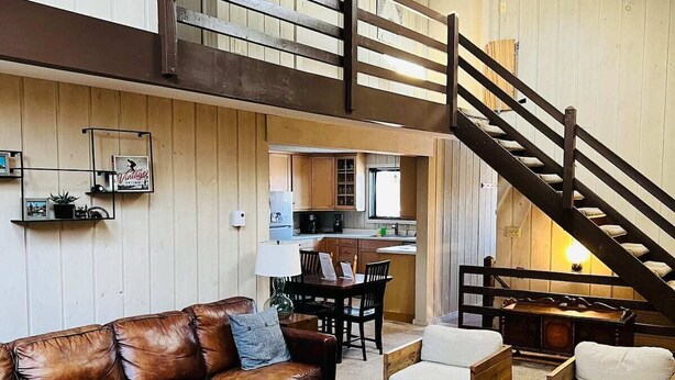 A spacious living area with a brown leather sofa, a wooden coffee table, and wicker chairs. A staircase leads to an upper level.