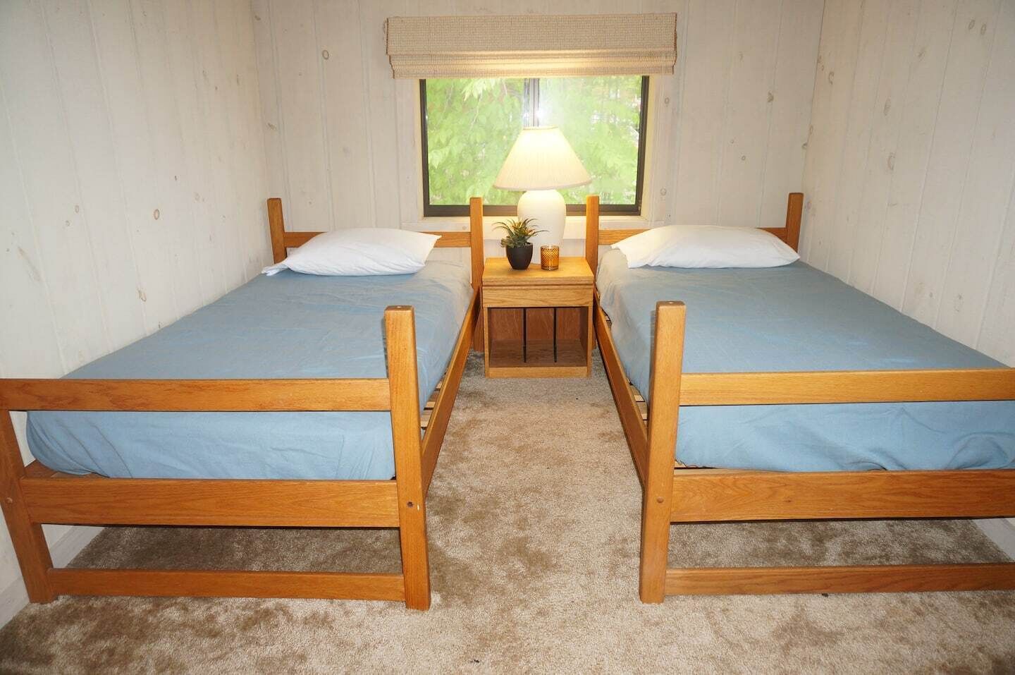 Une chambre avec deux lits en bois, une table de chevet avec une lampe et une fenêtre donnant sur un paysage verdoyant.