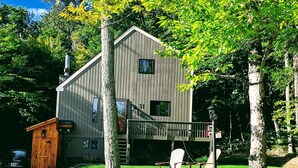 A two-story wooden house with a stone retaining wall, a covered porch, and a small shed.