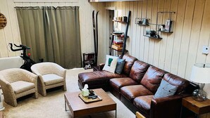 A cozy living room with a brown leather sofa, two wicker armchairs, a wooden coffee table, and a wooden chest.
