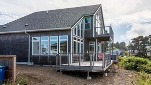 Moderni, kaksikerroksinen talo, jossa on suuret ikkunat, parveke ja puinen terassi.