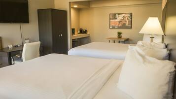 A hotel room with two beds, a desk, a TV, a wardrobe, and a painting on the wall.