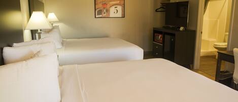 A hotel room with two beds, a TV, a desk, and a shower area.