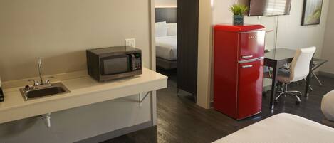 Een hotelkamer met een bed, een magnetron, een rode koelkast, een klein tafeltje met een stoel, een wastafel en een aan de muur bevestigde televisie.