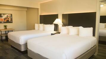 A hotel room with two beds, a nightstand with a lamp, a small table with a plant, and a painting on the wall.