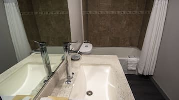 A bathroom with a double sink, a bathtub, and a toilet.