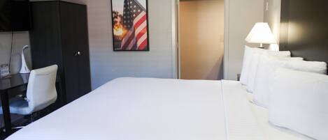 A hotel room with a large bed, a desk with a chair, a television mounted on the wall, and an American flag.