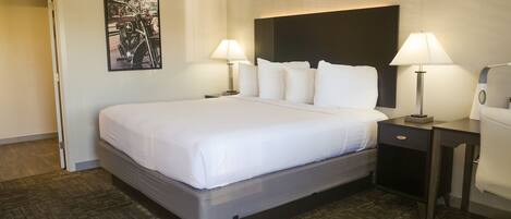 A hotel room with a large bed, two bedside tables with lamps, a headboard, a framed picture on the wall, and a carpeted floor.