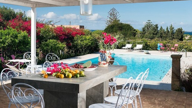 An outdoor pool area with a concrete bar, white metal chairs, and a table with fruit and flowers. - Villa Addolorata - Private villa near Marsala (Marsala)