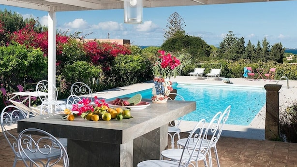 An outdoor pool area with a concrete bar, white metal chairs, and a table with fruit and flowers. - Villa Addolorata - Private villa near Marsala (Marsala)