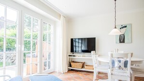 Une pièce lumineuse, dotée d’un téléviseur, de meubles blancs et d’une grande fenêtre.