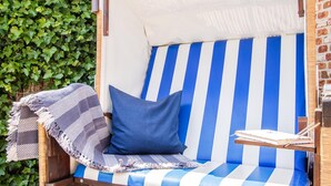 Un fauteuil à rayures avec un coussin, une petite table avec un livre et un stylo, et un mur de briques avec de la verdure en arrière-plan.