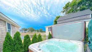 Un jacuzzi dans un jardin, avec une pelouse, une terrasse en bois et une maison en arrière-plan.