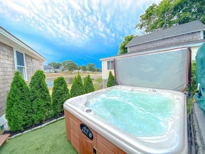 Ein Whirlpool in einem Garten mit Rasen, einer Holzterrasse und einem Haus im Hintergrund.