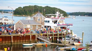 Un bateau amarré, une foule de personnes, un petit bâtiment et, au loin, une colline boisée.