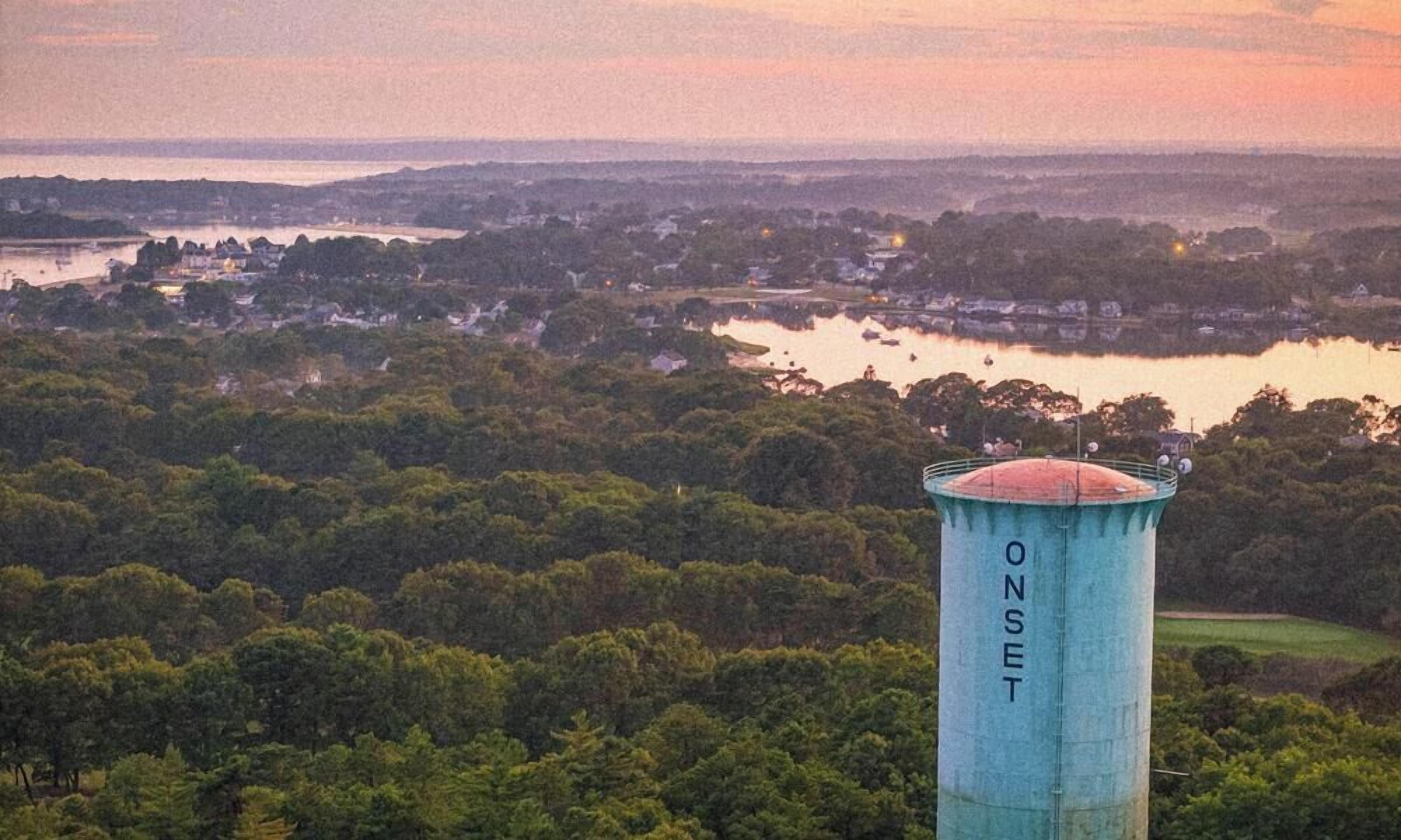 Un château d’eau portant l’inscription « ONSET », avec vue sur un lac et la forêt environnante.