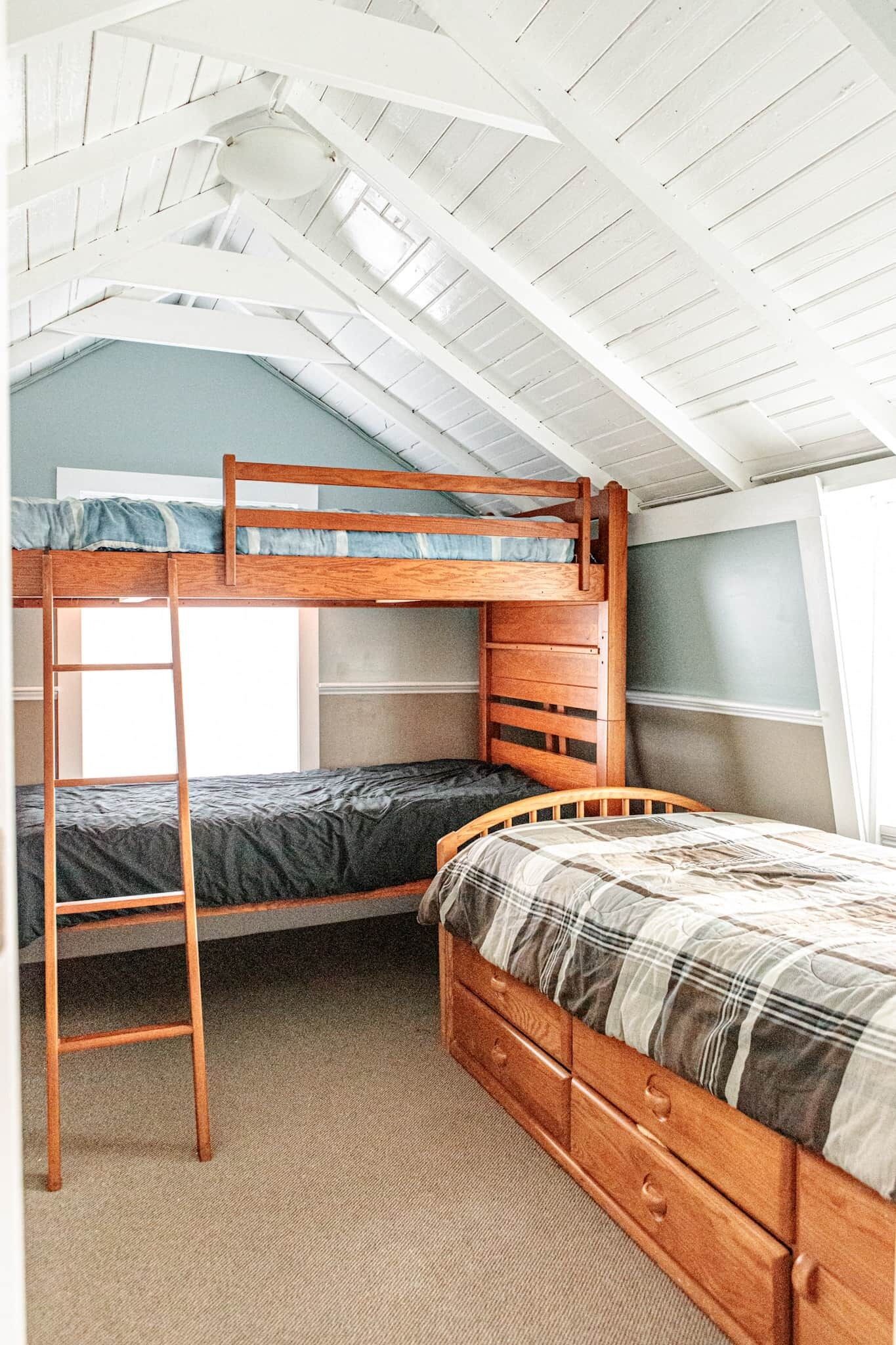 A dorm-style room with bunk beds, a ladder, and a window.