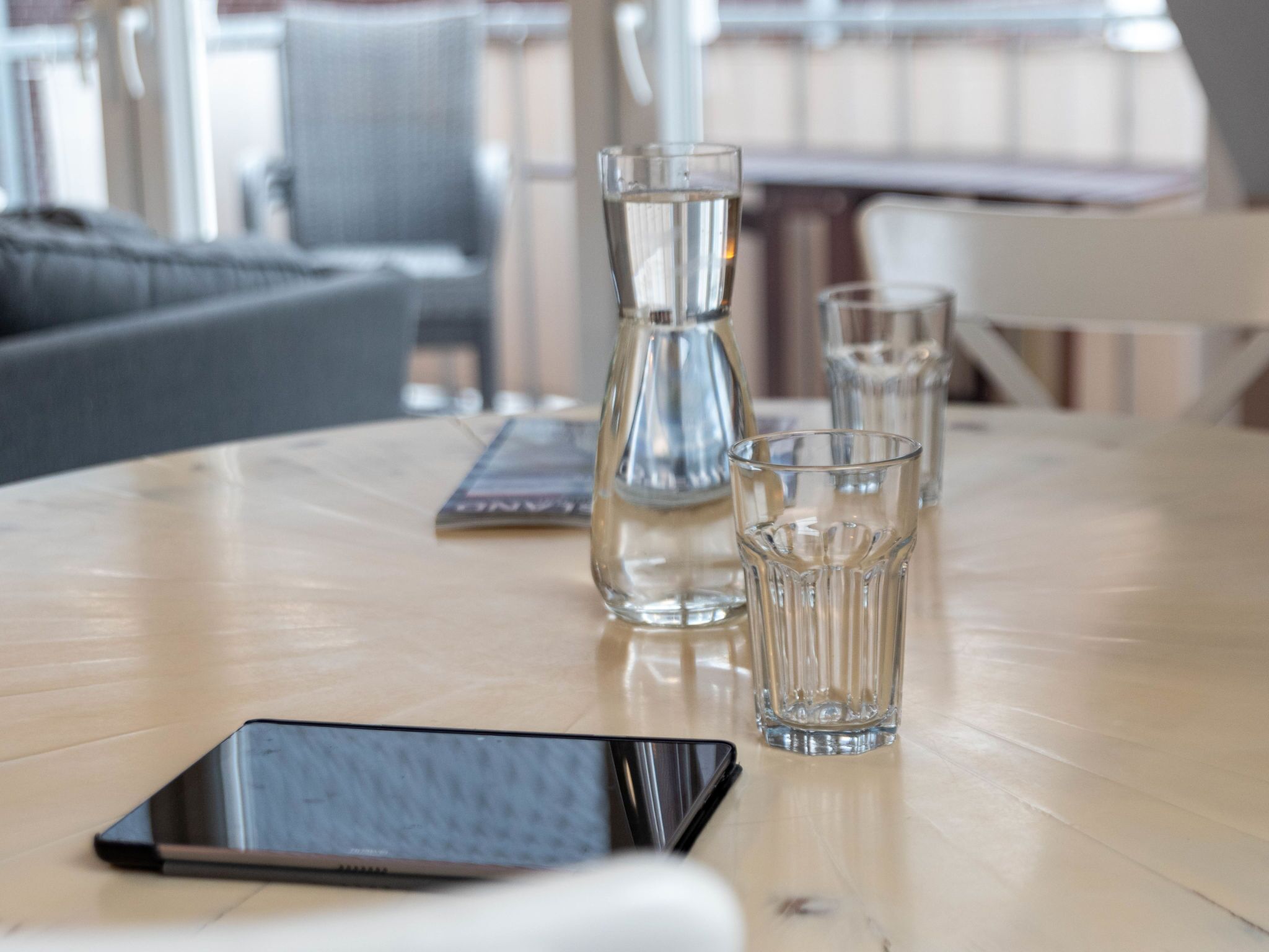 Een tafel met een smartphone, een glazen karaf en twee glazen op een houten ondergrond.