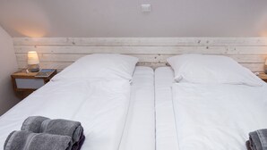 Ein Doppelbett mit weißen Leinen, zwei Kissen, ein Nachttisch mit Lampe und gefaltete Handtücher.