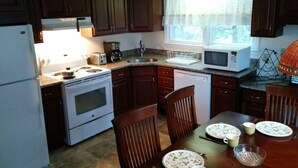A kitchen with wooden cabinets, a stove, a microwave, and a dining table set for four. - Lake House Located Near North Fork Wineries (Southold)