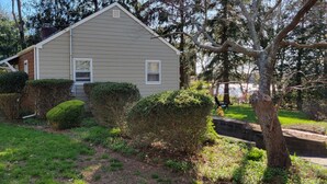 A single-story house with a beige exterior, surrounded by well-maintained hedges and trees. - Lake House Located Near North Fork Wineries (Southold)