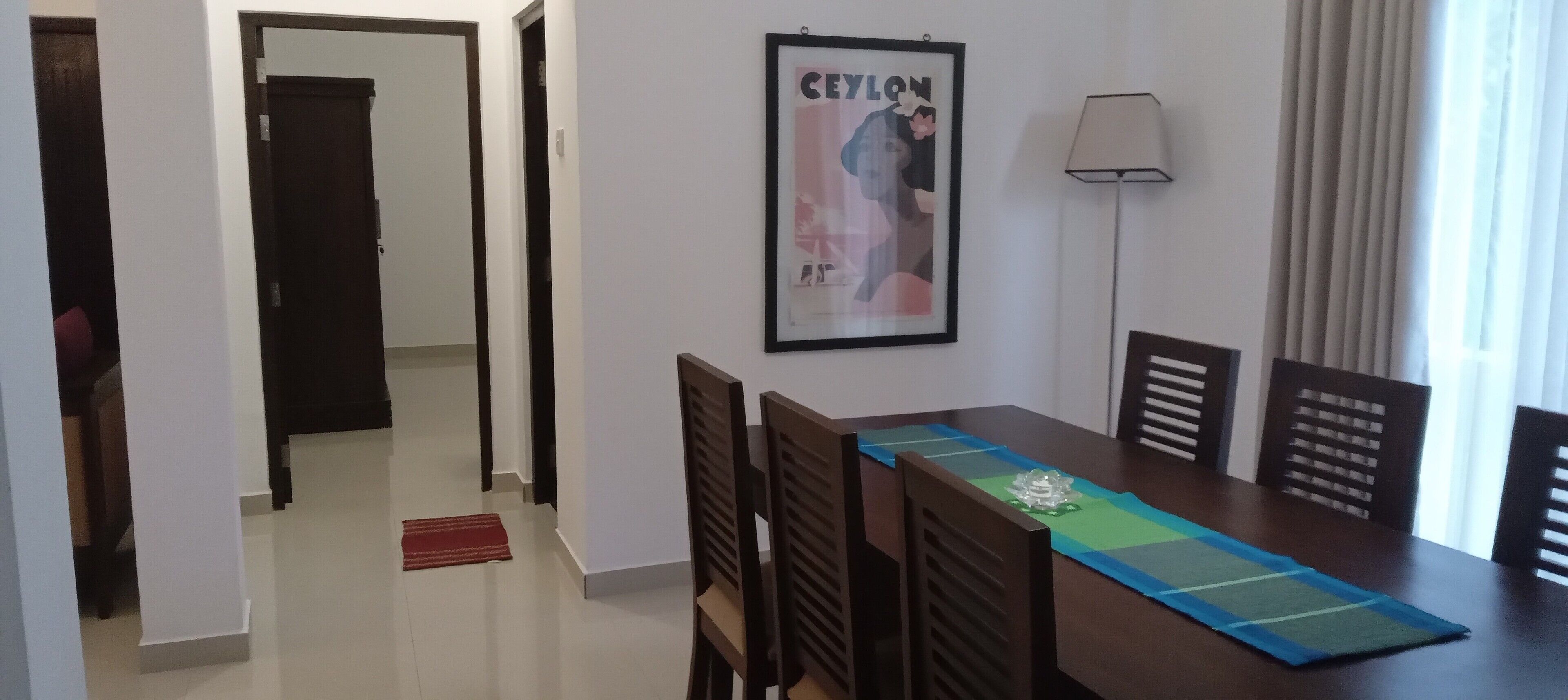 Un comedor con una mesa, sillas, un cartel enmarcado y una lámpara.