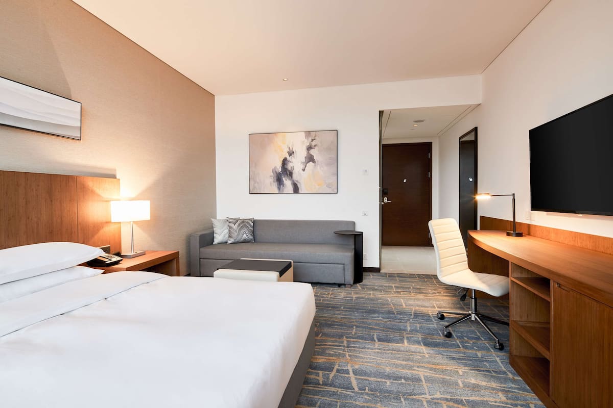 Habitación de hotel con una cama grande, un escritorio, una silla, un sofá y un cuadro en la pared.