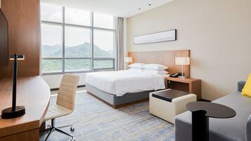 Une chambre d’hôtel équipée d’un lit, d’un bureau, d’une chaise et offrant une vue sur les montagnes grâce à de grandes fenêtres.