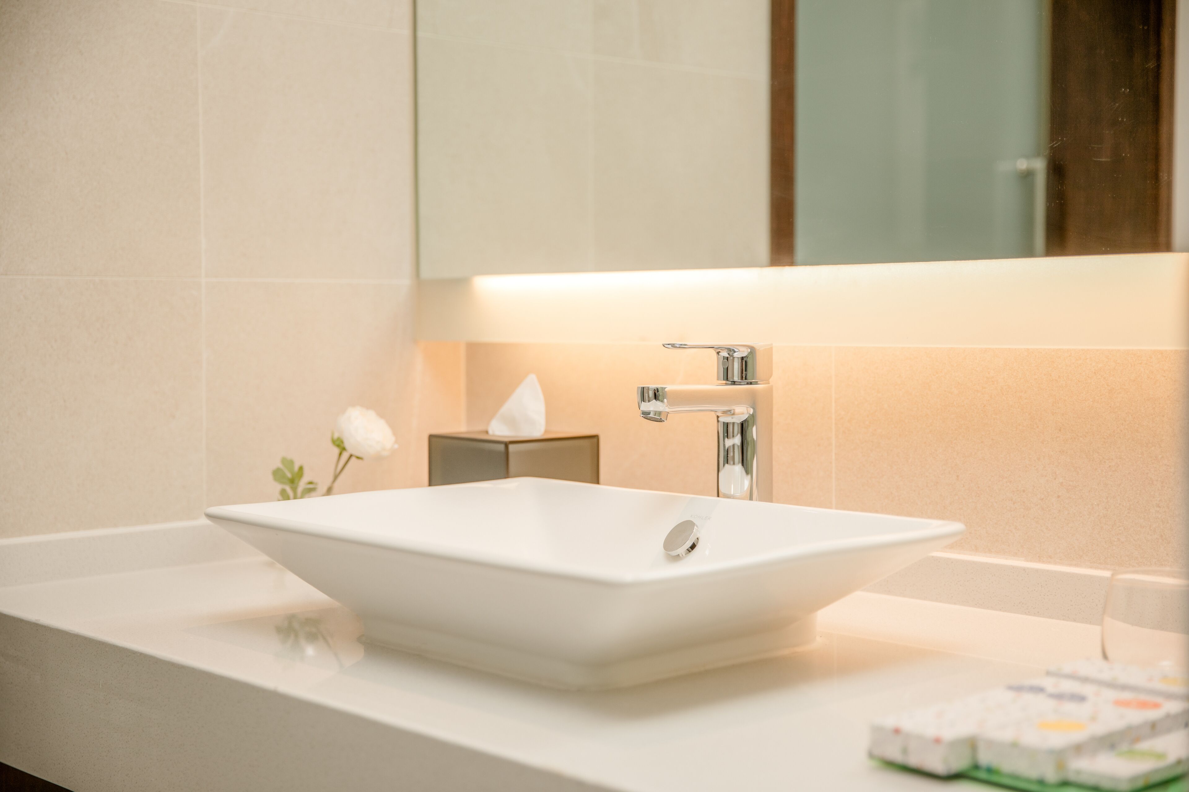 Un baño con lavamanos blanco, un espejo y dispensador de toallas.
