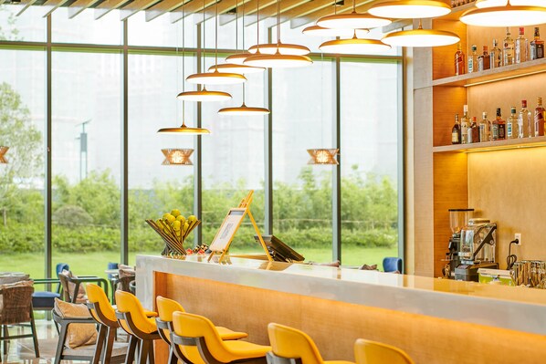 Zona de bar con sillas amarillas, una barra de madera y vistas a la vegetación a través de amplios ventanales.