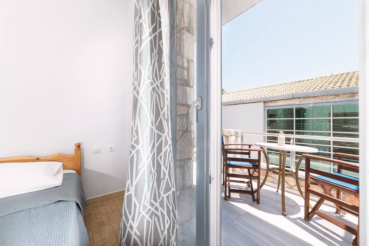 A balcony with a table and chairs, a bed with a wooden headboard, and a patterned curtain.
