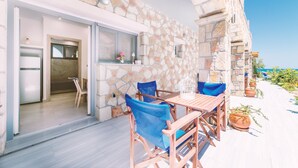 A stone-walled outdoor area with a wooden table and blue chairs, a door leading to an interior space, and potted plants. - Zakynthos-Summer Sea View (Zakynthos)