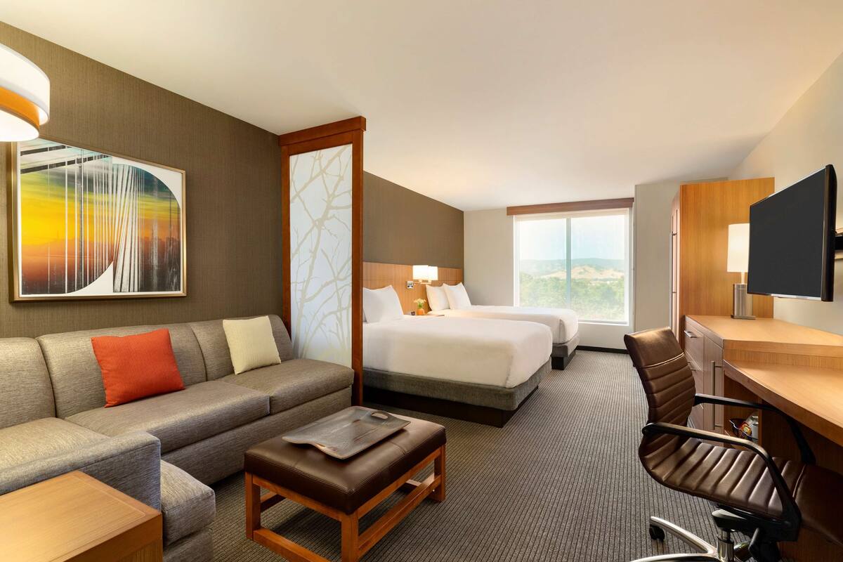 A hotel room with a sofa, a desk, a chair, a bed, and a TV.
