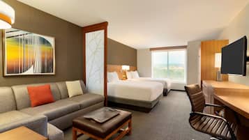 Ein Hotelzimmer mit Sofa, Schreibtisch, Stuhl, Bett und Fernseher.