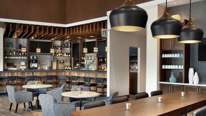 A modern bar area with wooden paneling, multiple seating options including round tables and bar stools, and a variety of bottles and glasses on shelves. - Hyatt Place Vacaville (Vacaville)