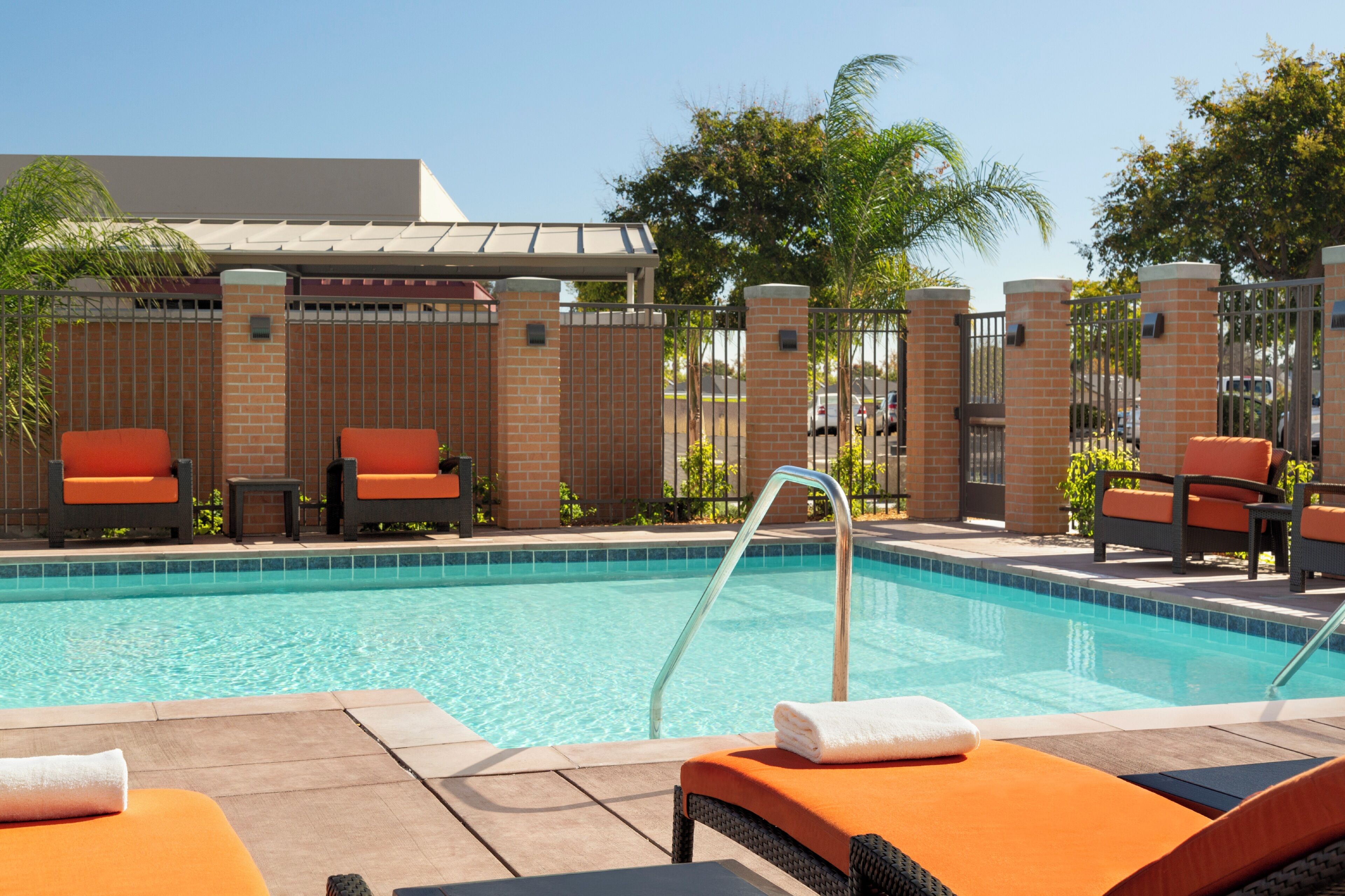 A poolside area with lounge chairs, a swimming pool, and a brick wall.