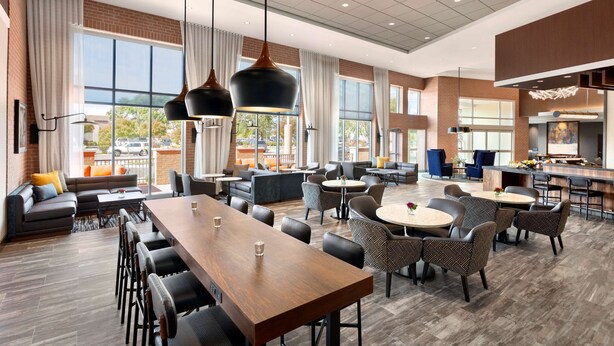 A spacious hotel lobby with a long wooden reception desk, multiple seating areas, and large windows offering views of the outside. - Hyatt Place Vacaville (Vacaville)