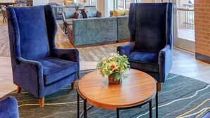 A modern hotel lobby with a seating area featuring blue armchairs, a round wooden table with a floral centerpiece, and a large chandelier. - Hyatt Place Vacaville (Vacaville)