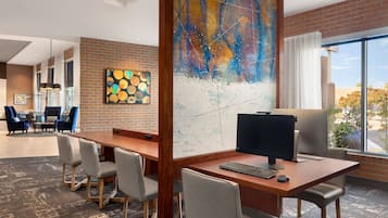 A modern office space with a large desk, computer, and multiple chairs. There is a large abstract painting on the wall and a map on the opposite wall.