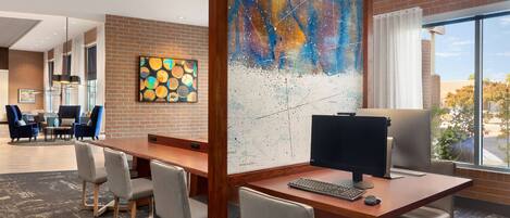 A modern office space with a large desk, computer, and multiple chairs. There is a large abstract painting on the wall and a map on the opposite wall.