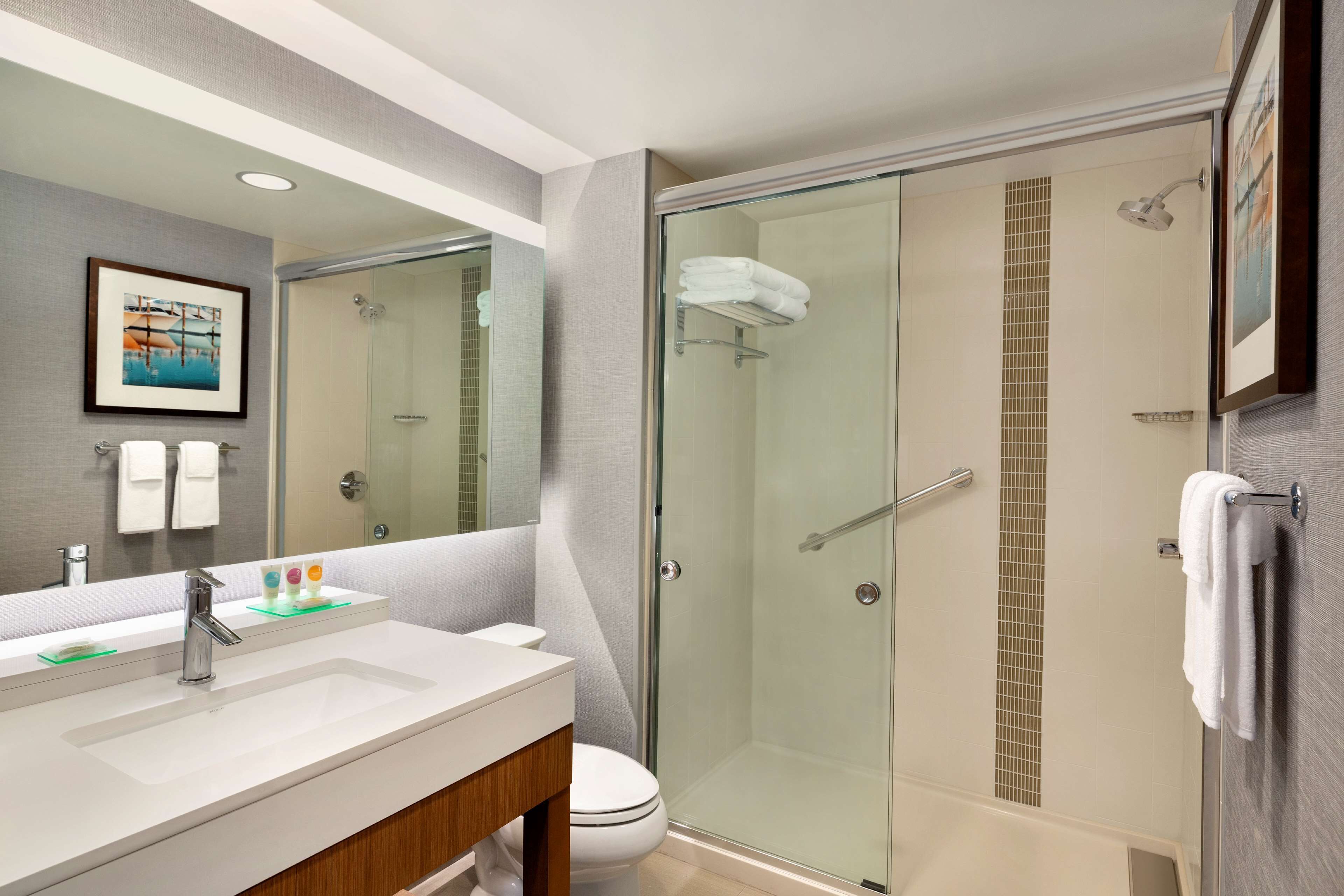 Un baño moderno con ducha envuelta en vidrio, un espejo grande y un lavabo blanco con tocador.