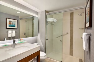 Un baño moderno con ducha envuelta en vidrio, un espejo grande y un lavabo blanco con tocador.
