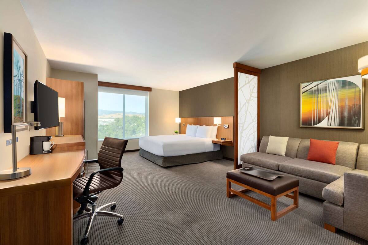 A hotel room with a bed, a desk, a chair, a sofa, and a TV.
